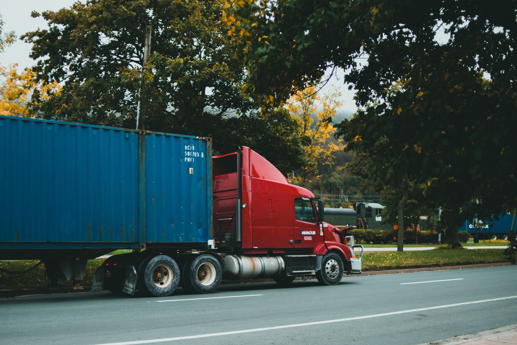 American semi truck carrying a shipping container on a tree-lined road